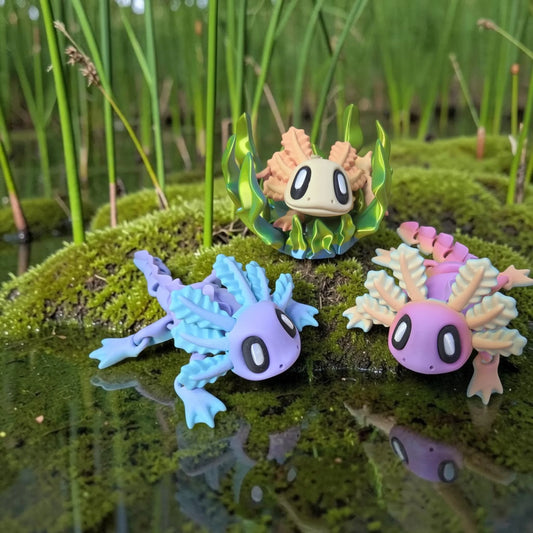 HPHobbies Blob Axolotl articulated figures in blue, pink, and peach resting on a mossy pond surface with seaweed