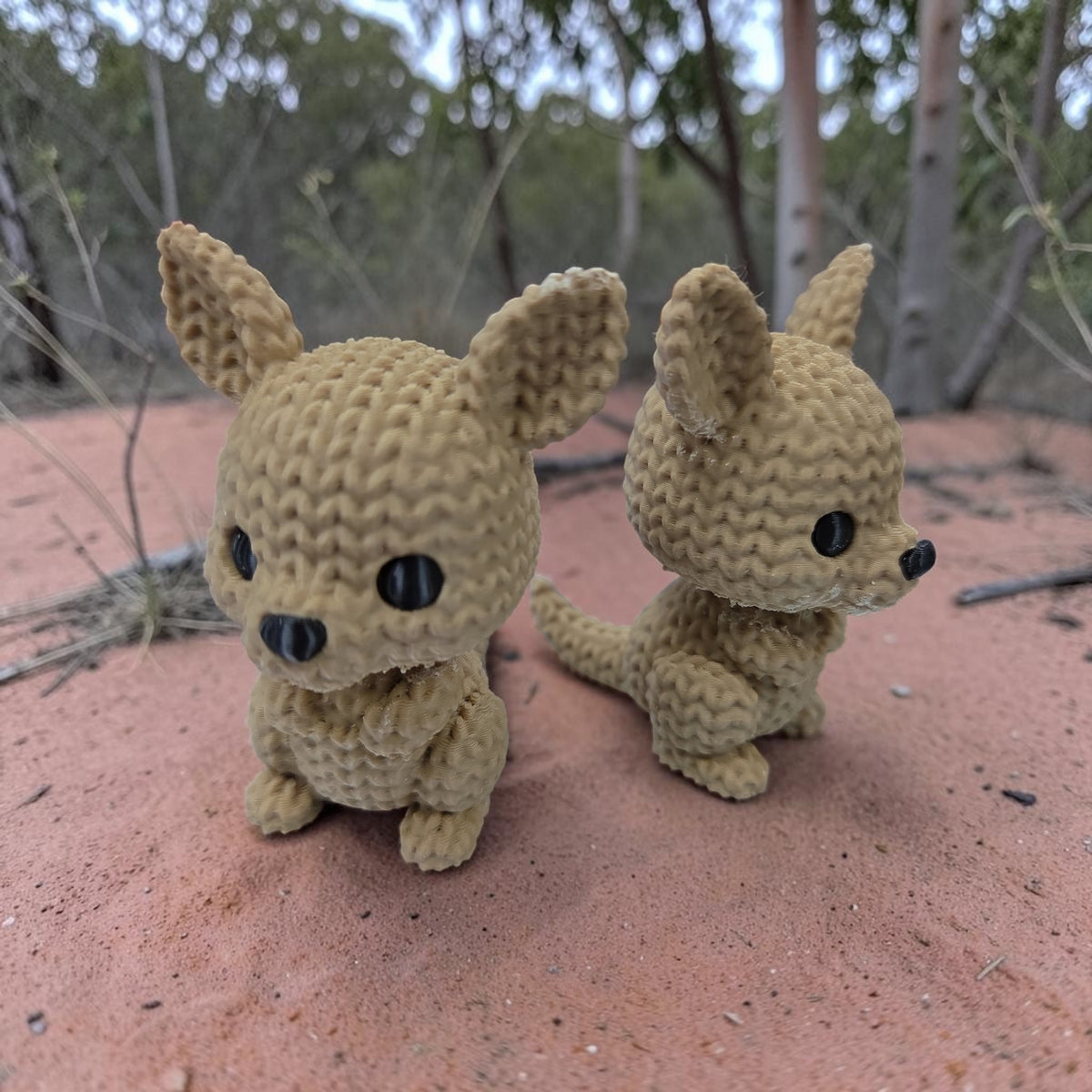 Two HPHobbies faux knit kangaroo figurines with realistic crochet-style texture standing on red dirt outdoors.