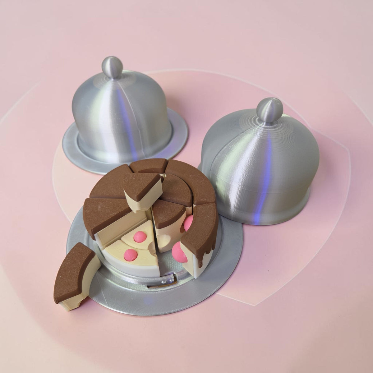HPHobbies layered cake puzzle with silver cloche covers on a pink surface, featuring brown and cream 3D printed parts.